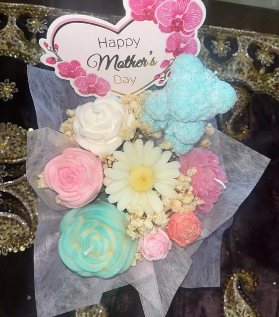A Mother's Day candle bouquet with a blue bear, a white daisy, pink and teal roses and a Happy Mother's Day card