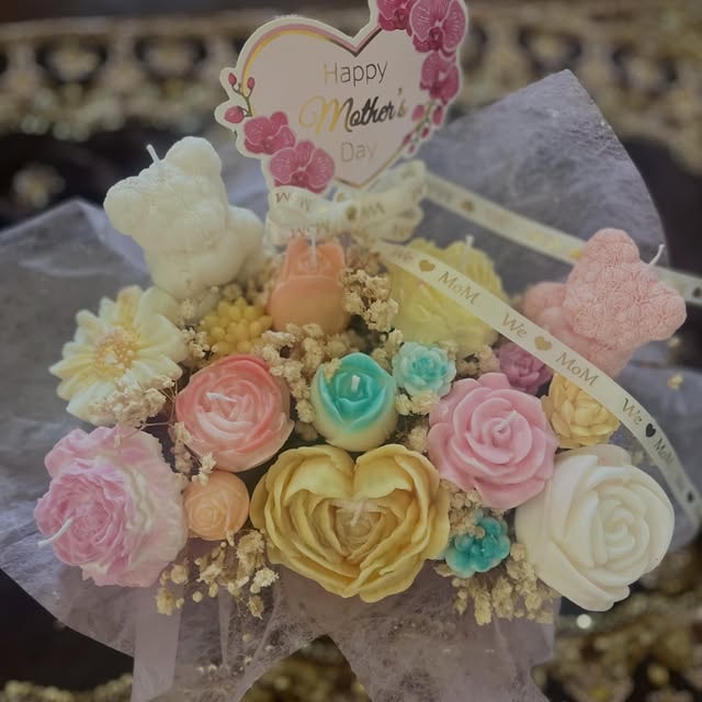 A bouquet of handmade flower candles: a white bear candle, a yellow heart rose, pink and teal roses and a daisy, wrapped in lace with a Happy Mother's Day card