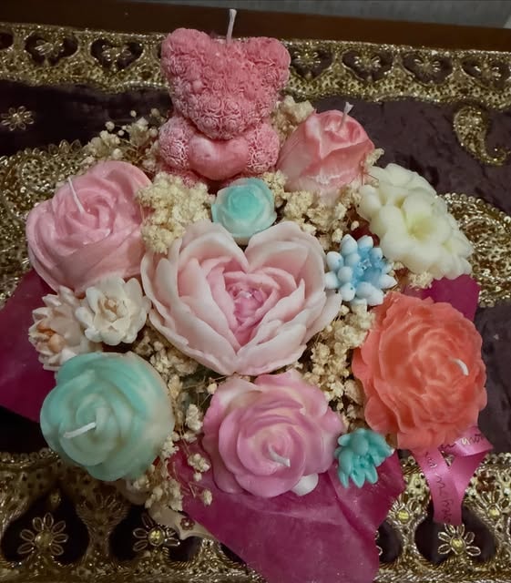 A candle bouquet with a pink bear, a heart shaped pink rose, an orange peony and teal and white flowers, handmade candles