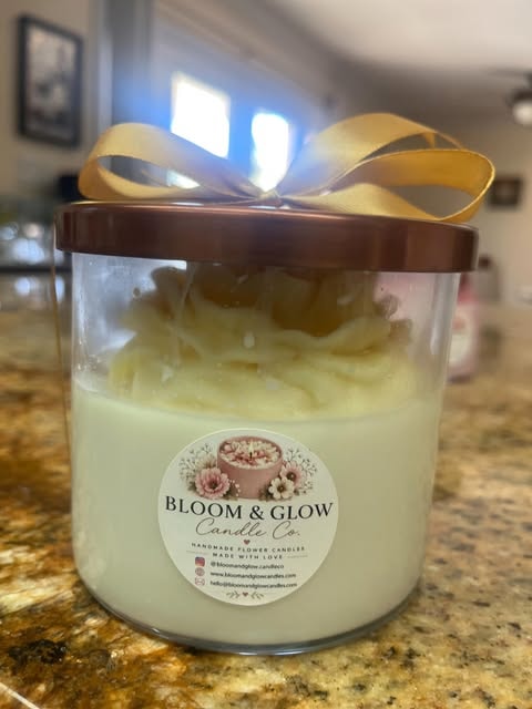 A green handmade flower candle jar with a bronze lid and a gold bow, wearing a Bloom and Glow Candle Co. label